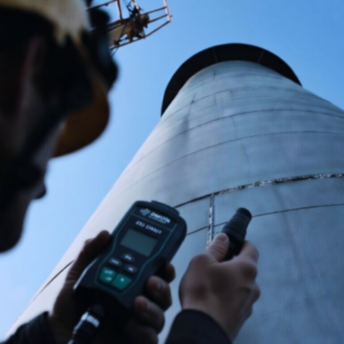 Technicien de Construction Inspectus mesurant l'épaisseur d'acier par ultrasons sur une cheminée industrielle